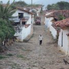 Photo of elderly person walking through a cobbled street with a cat in the foreground